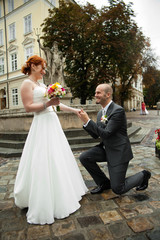 Wall Mural - Happy groom stands on the knee in the front of a bride in the mi