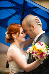 Wall Mural - Bride and groom lean to each other standing undet the umbrella