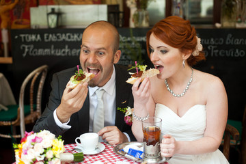 Wall Mural - Bride and groom eat sandwiches sitting at the table in street ca