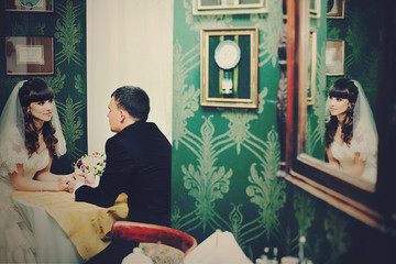 Stylish wedding couple sits in the green restaurant hall