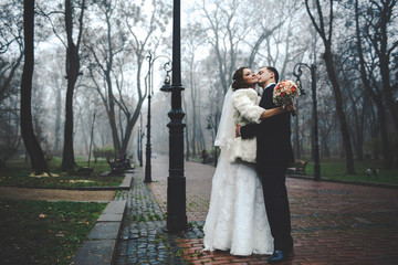 Groom kisses bride's neck standing in the foggy autumn park