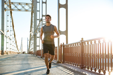 Poster - Attractive fit man running along bridge at sunset light