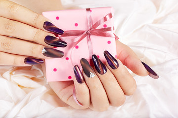 Wall Mural - Hands with long artificial manicured nails holding a gift box with bow