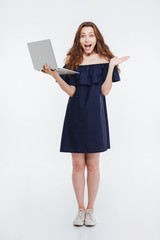 Wall Mural - Happy excited young woman standing and holding laptop