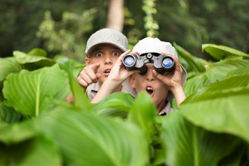 excited young campers hiding in grass looking through binoculars