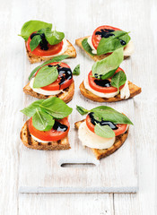 caprese sandwiches with tomato, mozzarella cheese, basil and balsamic glaze on white painted board o