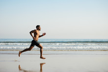 Black Fit Man Running Barefoot By The Sea On The Beach. Powerful Runner Training Outdoor On Summer.