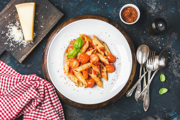 Wall Mural - Pasta penne with tomato sauce, basil and roasted tomatoes served with parmesan cheese. Old painted dark plywood background, top view, horizontal composition