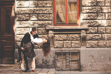 Wall Mural - Young man bends pretty brunette over standing on the old street