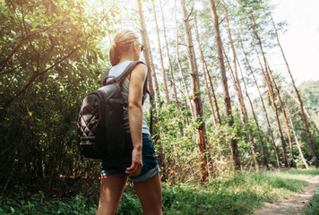 Young active woman hiking across natural park on the trail. Female backpacker traveling in summery forest. 