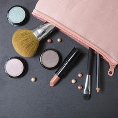 Wall Mural - A pastel pink make up bag with cosmetic products spilling on a dark slate background