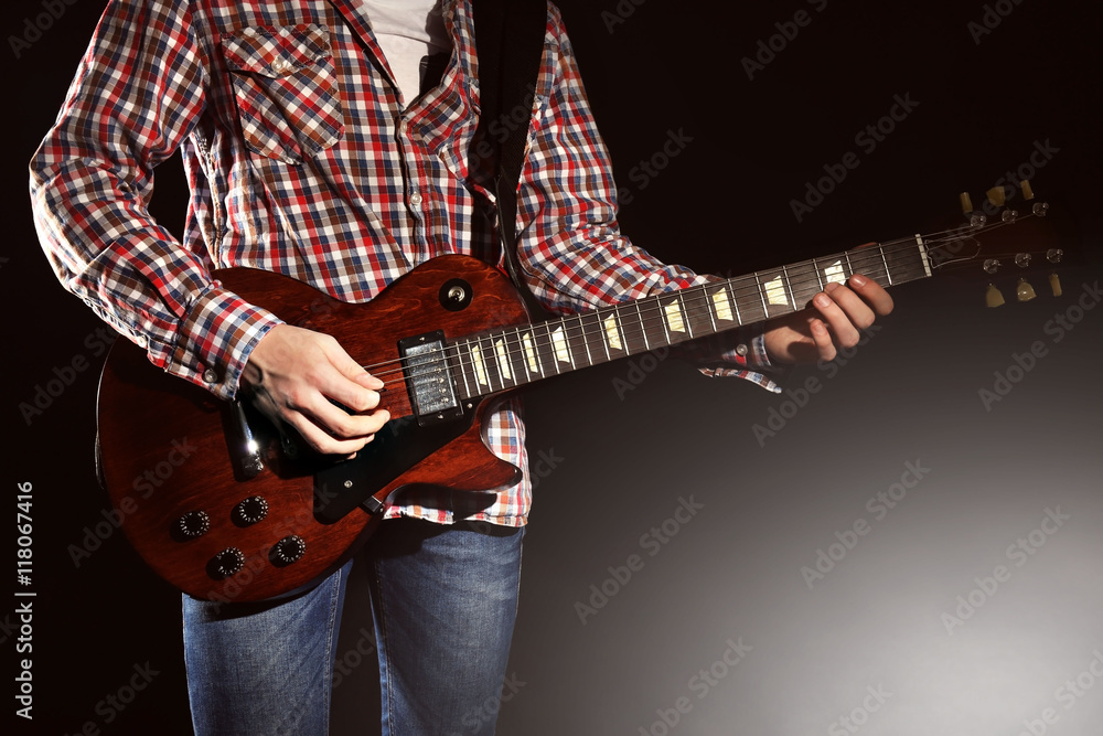 Young man playing electric guitar on lighted dark background