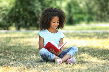 Wall Mural - Cute girl reading book on green grass