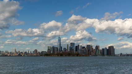 Fototapete - Time lapse of New York City’s Lower Manhattan Financial District skyscrapers and clouds with Ellis Island from New York harbor