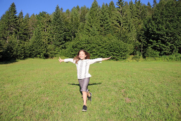 Wall Mural - happy little girl running on green grass field