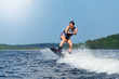 Slim brunette woman riding wakeboard on motorboat wave in lake