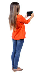 Canvas Print - back view of standing young beautiful  woman  using a mobile phone. girl  watching. Rear view people collection.  backside view of person.  Isolated over white background. girl in a red jacket holding