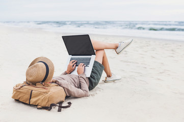 Wall Mural - Young woman using laptop computer on a beach. Freelance work, e-learning, social distancing, distance work, connection concept