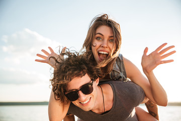 Poster - Young happy smiling couple in love piggyback at the beach