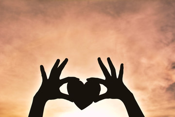 Wall Mural - Silhouette hand holding heart shape sunset background. concept love