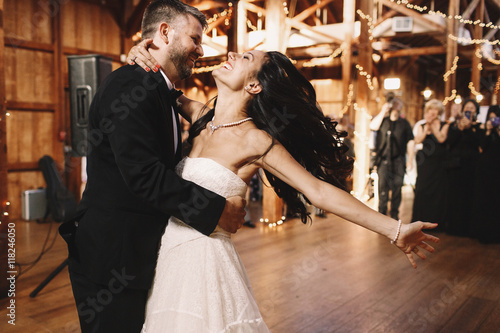 Fotografía Bride shakes her dark hair while dancing with a groom in wooden