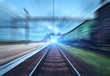 Railway station with cargo wagons and train light in motion at sunset. Railroad with motion blur effect. Railway platform. Heavy industry. Conceptual background