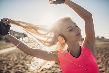 Portrait of young beautiful woman listening to music at beach. Close up face of smiling blonde woman with earphone looking at camera. Girl running at beach and listening to music.