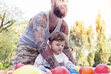 tattooed father have fun with his son in the park with colored b