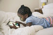 © Hello Lovely/Blend Images - African American girl using digital tablet on bed