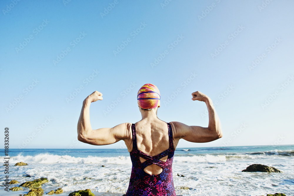 Senior woman flexing her muscles on beach