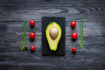 Veggie Food composition with half avocado over a darkdish