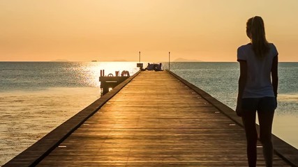 Wall Mural - Young woman walking on the pier by the sea at sunset background