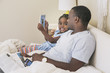© Hello Lovely/Blend Images - African American father and daughter using digital tablet on bed
