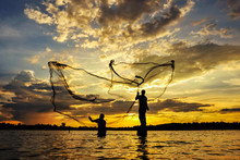 Silhouette  Fisherman Casting A Nets Into The Water During Sunset.