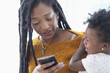 © JGI/Tom Grill/Blend Images - Black woman holding baby daughter using cell phone