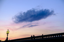 Blue Fluffy Cloud On Evening Sky Above Bridge With Tourists
