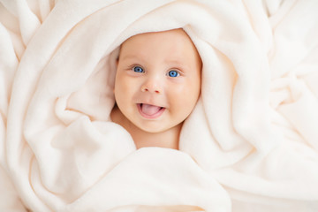 Caucasian baby boy covered with  towel joyfully smiles at camera