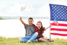 Boy And Girl Holding American Flag On River Bank