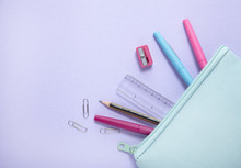 An Aerial View Of A Blue Pencil Case With Stationery Spilling Out On To A Pastel Purple Background, Forming A Page Border