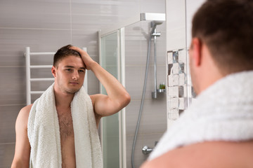 Wall Mural - Handsome male holding towel on his shoulders while looking in th