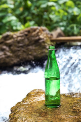 Wall Mural - Green bottle on small waterfall background