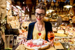 © rh2010 - Young woman sitting near the food shop with traditional italian appetizer on the blurred food showcase background in Bologna city. Bologna is the gastronomic center of Italy