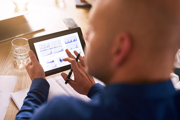 Portable computer tablet being used by a caucasian male business executive during a board meeting to view live analysis of the company's investment portfolio.