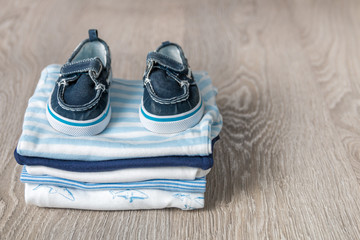 Folded blue and white bodysuit with shoes on it on grey wooden background. diaper for newborn boy. Stack of infant clothing. Child outfit. Copy space.