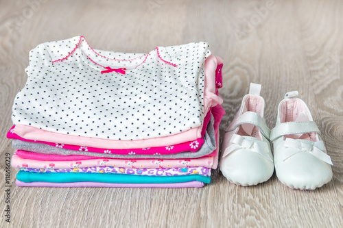 Zdjęcie XXL Fałdowy różowy i biały bodysuit z butami na nim na szarym drewnianym tle. pieluszka dla noworodka dziewczynki. Stos odzieży niemowlęcej. Strój dziecka. Ścieśniać.