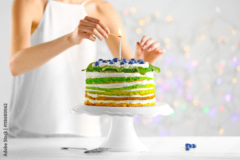 Woman decorating delicious cake on light background