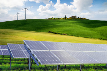 solar panels and wind turbines next to a farm house, against hil