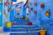 canvas print picture - Blue staircase and wall decorated with colourful flowerpots, Chefchaouen medina in Morocco.