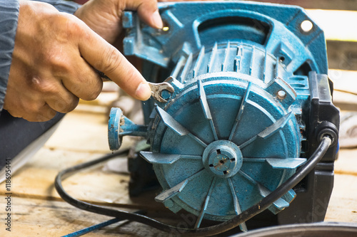 Fotografia, Obraz Electric motor and man working equipment repair on wooden floor background