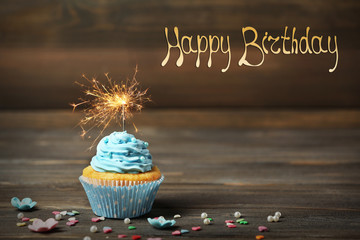 Sticker - Birthday cupcake with sparkler on wooden background